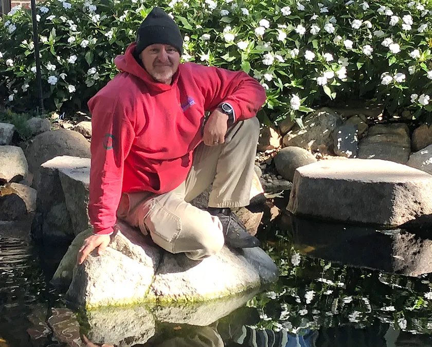 Person in garden sitting on rocks by pond.