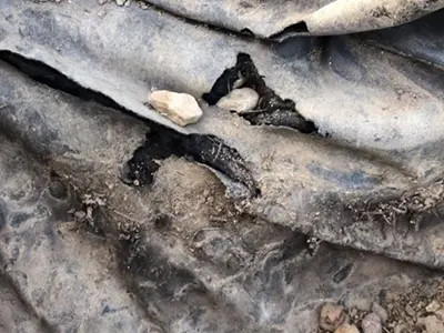 Torn tarp on ground with visible rocks underneath