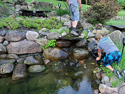 Two people maintaining a stone garden pond.