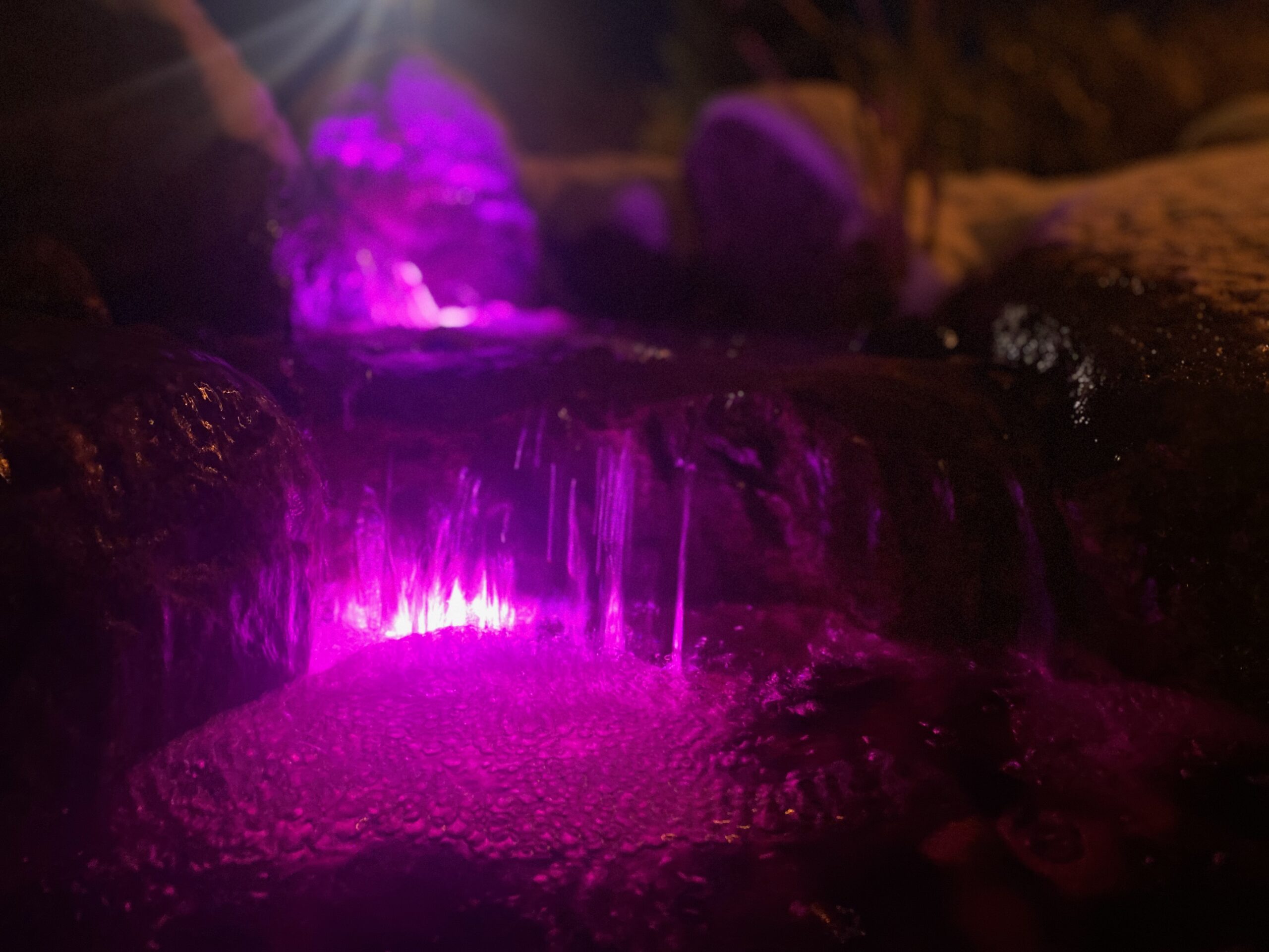 Waterfall illuminated with purple lights at night.