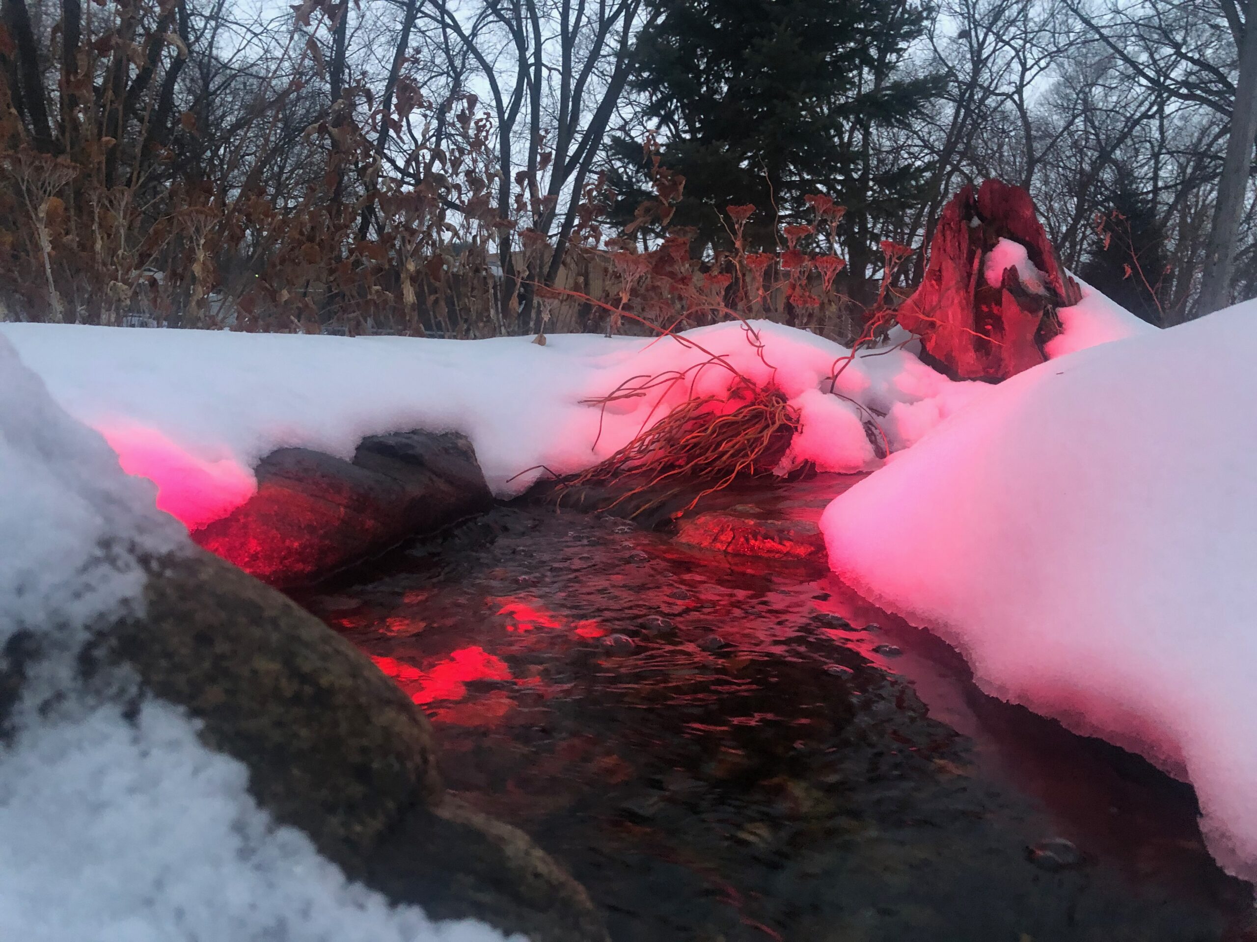 Snowy stream illuminated by red light at dusk.