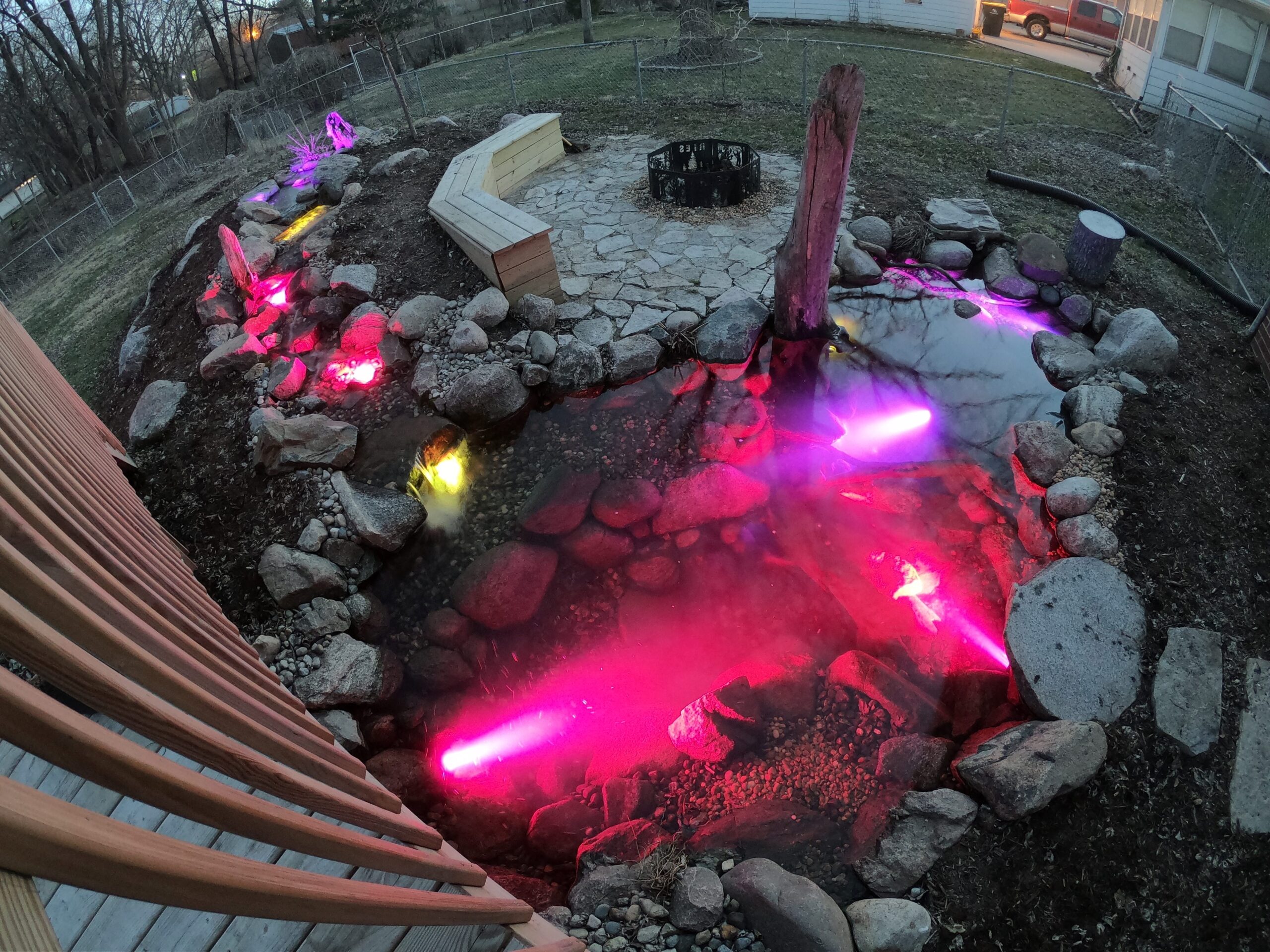 Colorful lights illuminate backyard pond with stones.